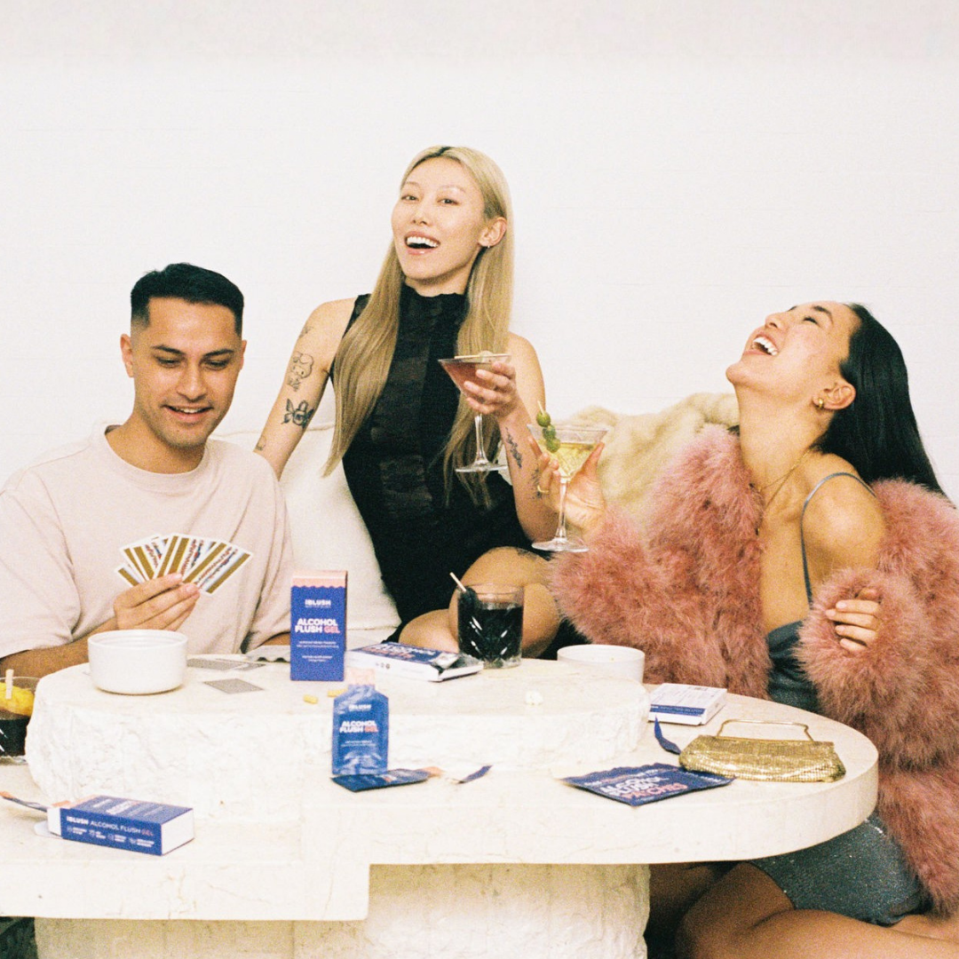Three people sitting around a table with drinks and cards, laughing and enjoying themselves.