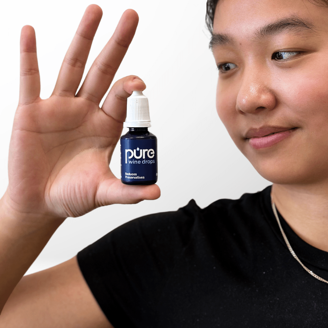 Woman holding PureWine Drops bottle, designed to reduce sulfites and prevent wine headaches and allergy symptoms.