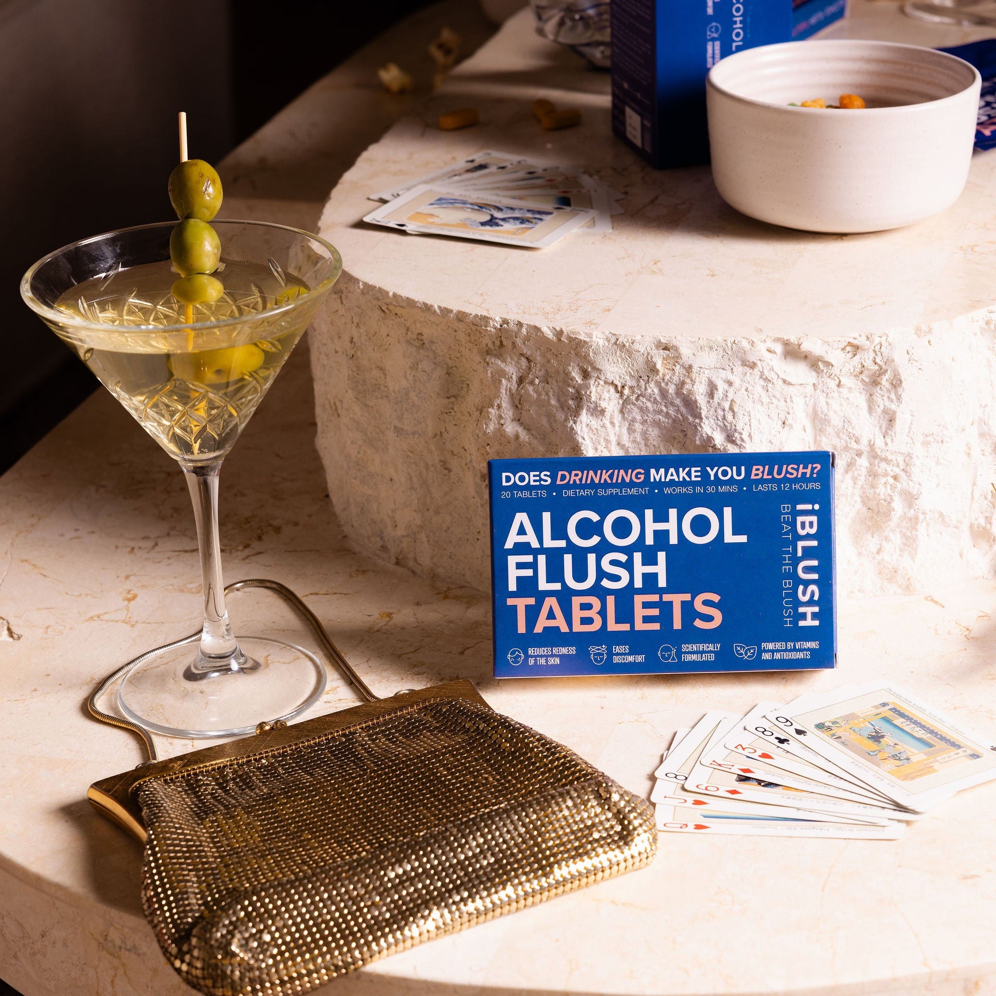 Alcohol flush tablets packaging on a table with a cocktail and clutch.
