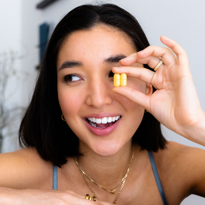 A smiling woman holding two yellow iBLUSH tablets, emphasizing the ease of use and effectiveness of the supplement.