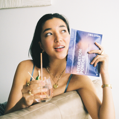 Woman on film holding iBlush Hydration Powder pouch, a sugar-free electrolyte powder designed to support hydration and recovery while drinking.